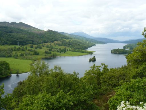 Blick vom Queen's View in Schottland auf Loch Tummel, einen See umgeben von grünen Hügeln und sanften Bergen.