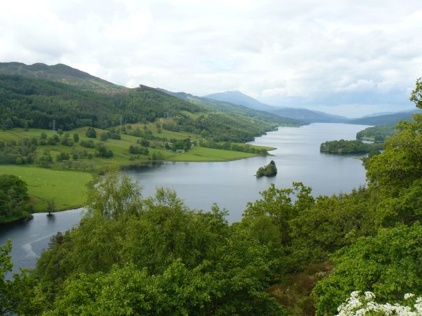 Blick vom Queen's View in Schottland auf Loch Tummel, einen See umgeben von grünen Hügeln und sanften Bergen.