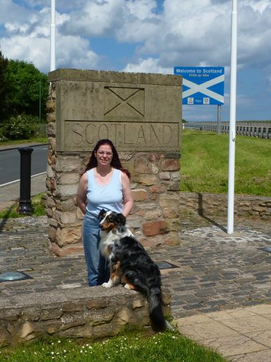 Elke mit Hund vor dem Stein und Schild an der Grenze zu Schottland